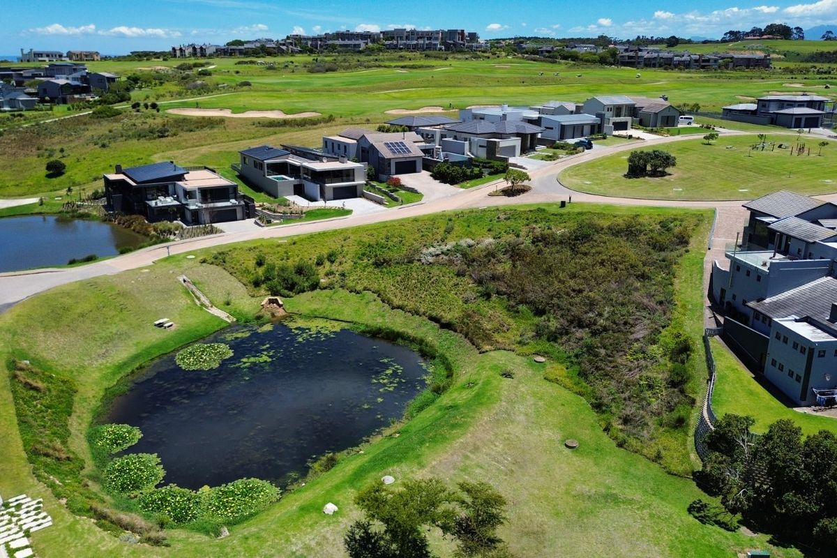 Aerial view of a residential estate featuring a vacant plot of land adjacent to a natural pond and surrounding modern homes.