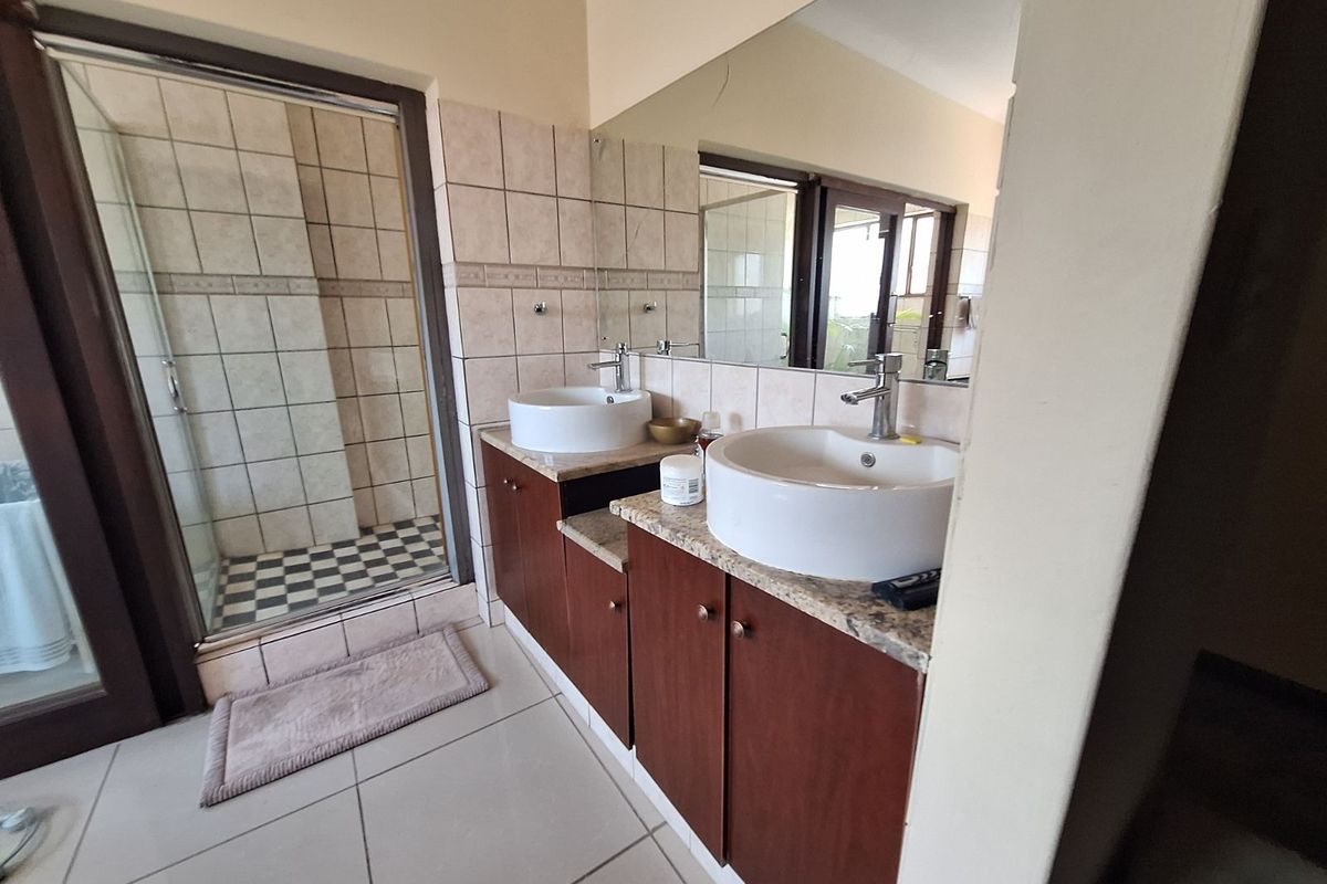 A functional bathroom featuring a double vanity with granite countertops, vessel sinks, and a separate glass-enclosed shower with tiled finishes.