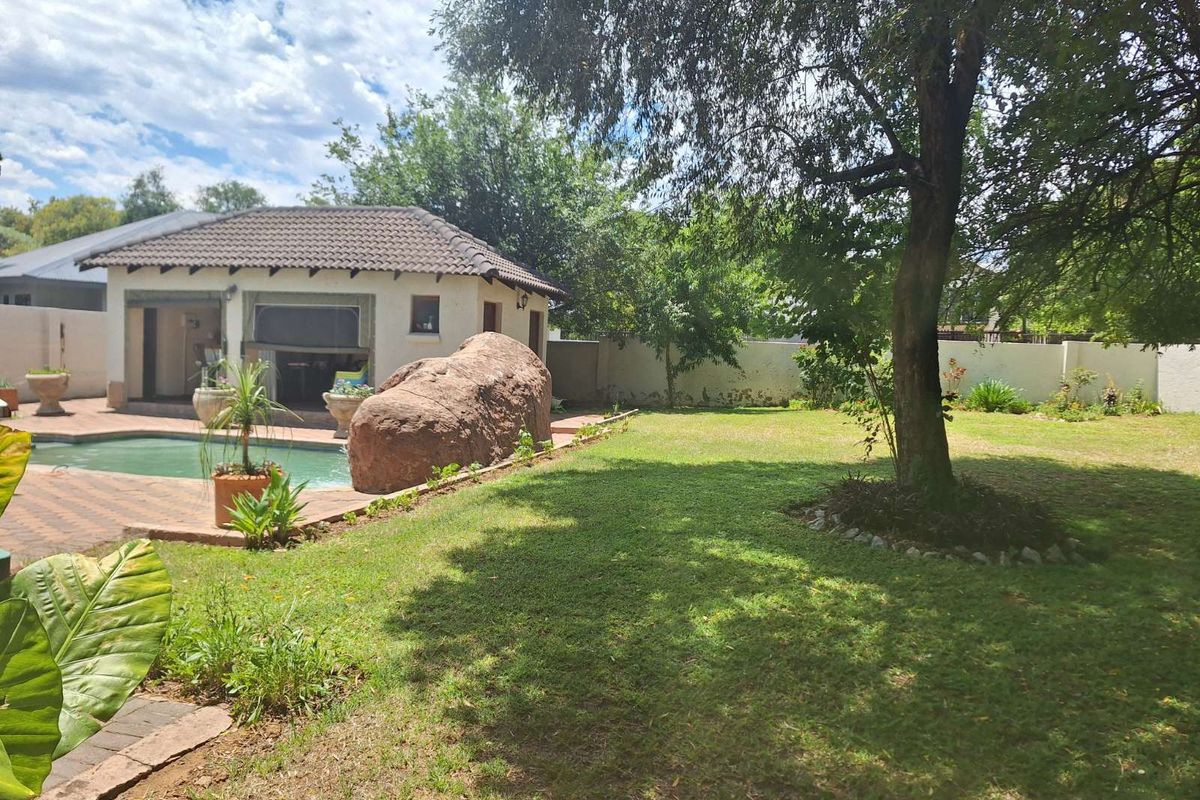 A spacious backyard featuring a swimming pool, a paved patio area, and a detached outbuilding, set within a well-maintained garden with mature trees.