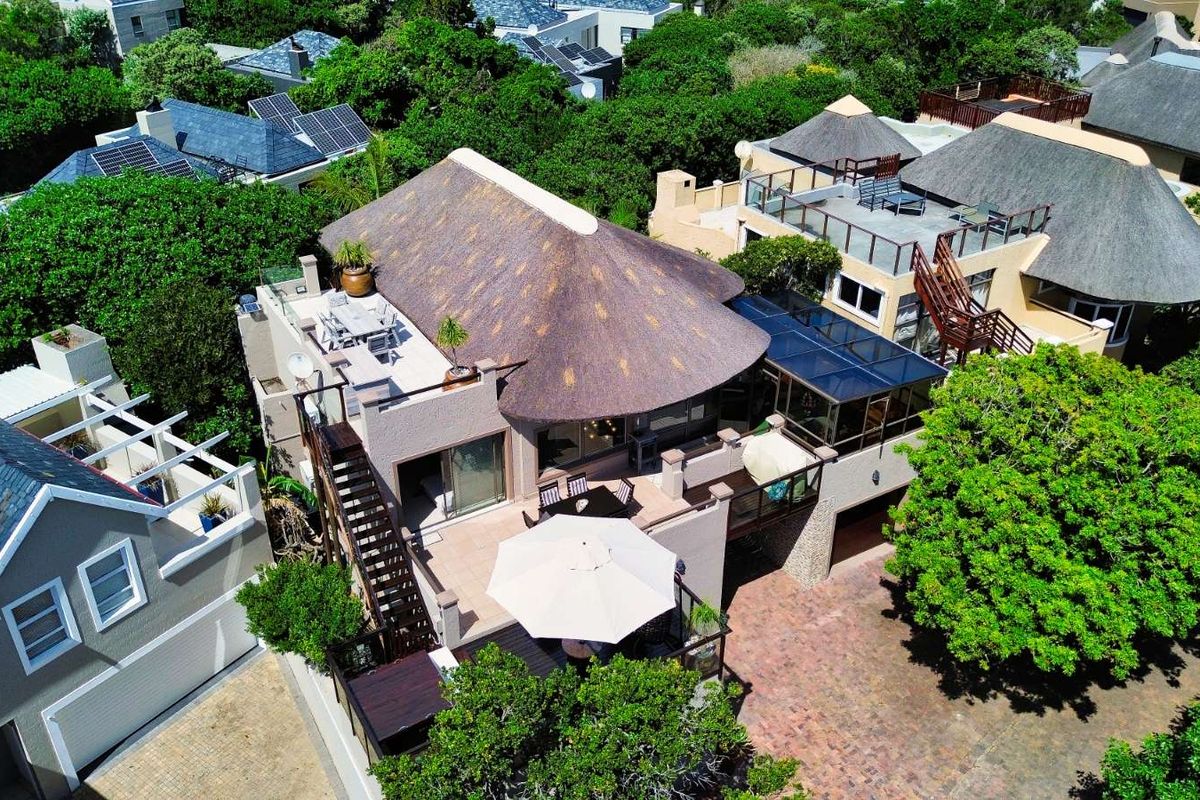 Aerial view of a multi-level residential property featuring a thatched roof, expansive outdoor terrace areas, and a paved driveway.