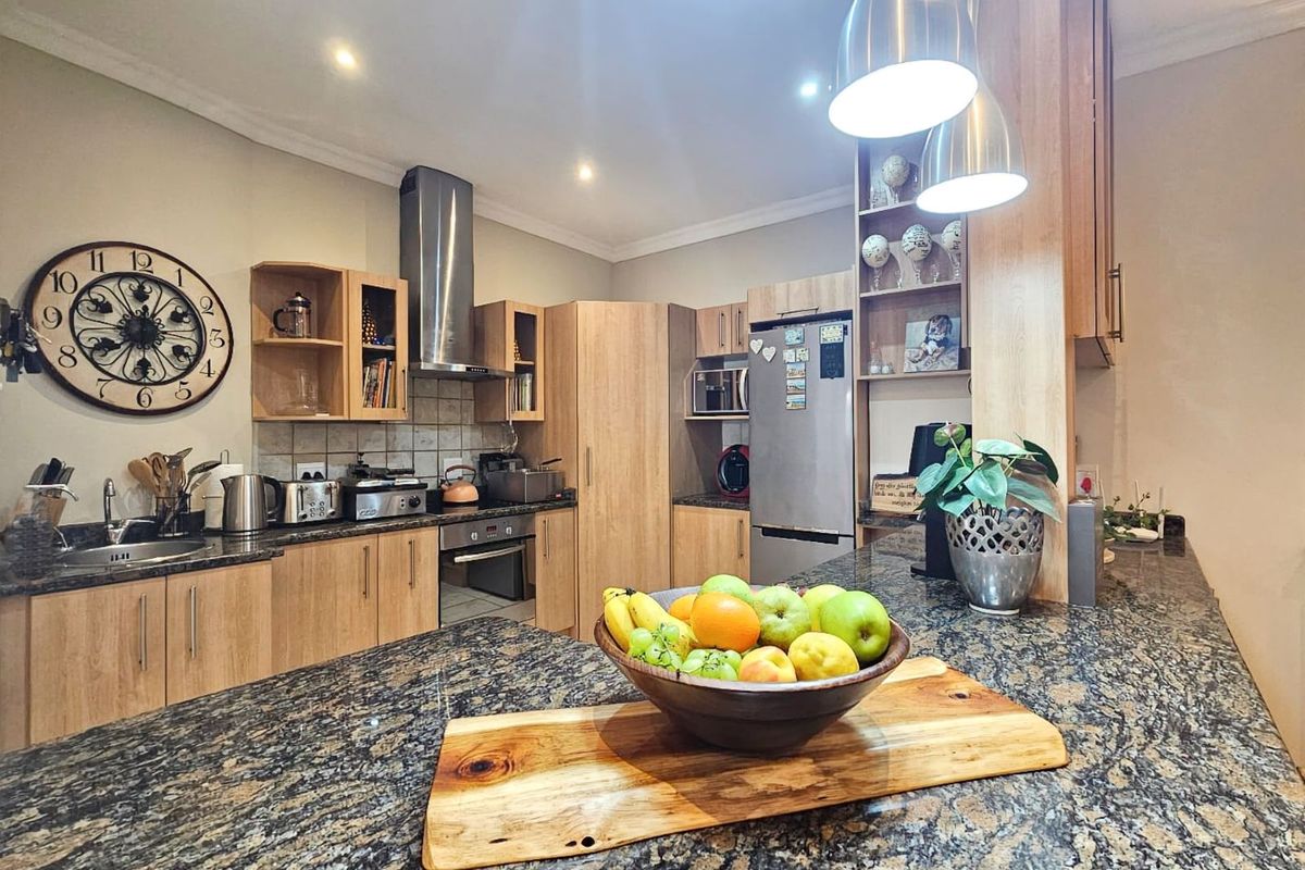 Modern kitchen featuring light wood cabinetry, dark granite countertops, stainless steel extractor fan, and integrated oven, offering a functional and well-maintained cooking space.