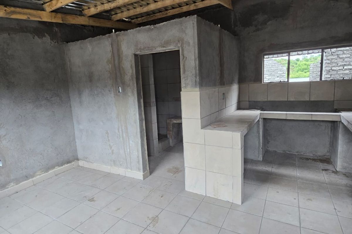 An unfinished kitchen area featuring tiled countertops, exposed concrete walls, and an open timber roof structure, awaiting final finishes and installation.