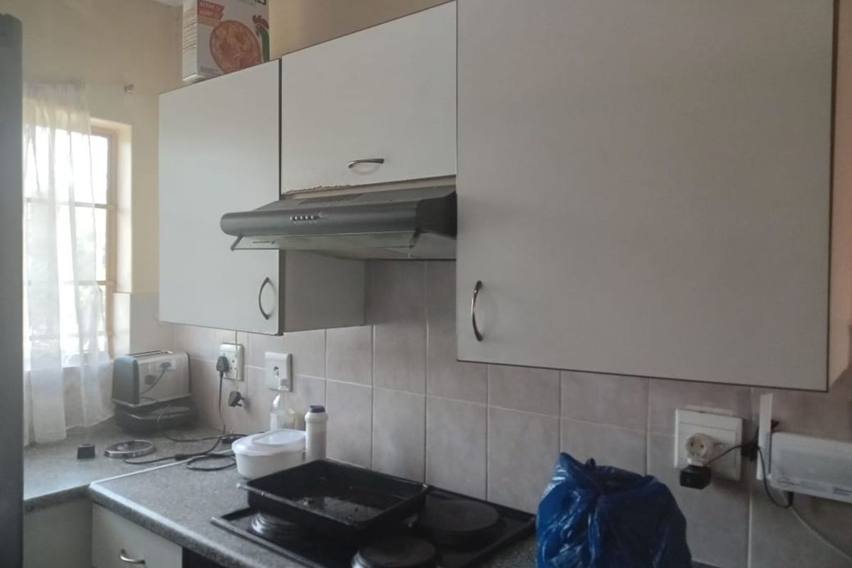 A functional kitchen featuring white cabinetry, a built-in extractor fan, a four-plate electric hob, and tiled splashbacks with ample counter space.