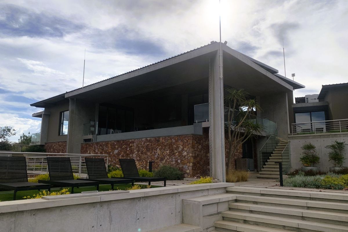 Modern architectural exterior featuring stone cladding, concrete structure, and a spacious covered patio area with glass balustrades overlooking the landscaped grounds.