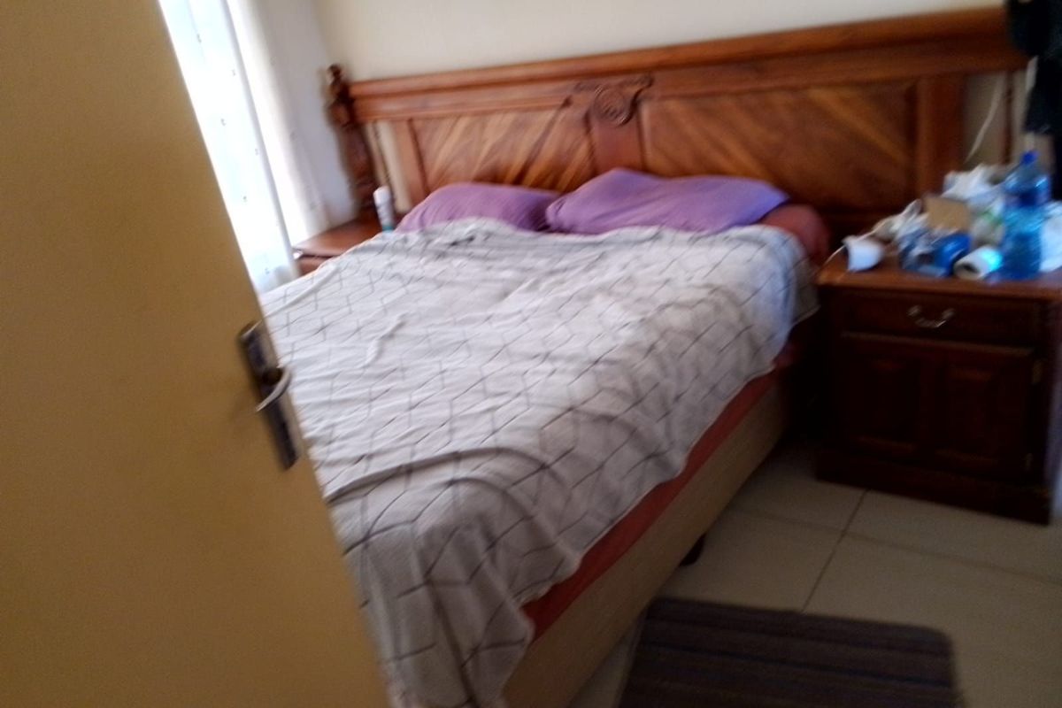A bedroom featuring tiled flooring and a wooden headboard, captured from the doorway.