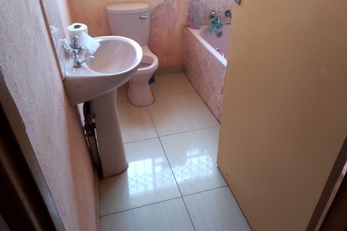 A compact bathroom featuring a pedestal basin, toilet, and bathtub with dated finishes and visible wall surface deterioration.