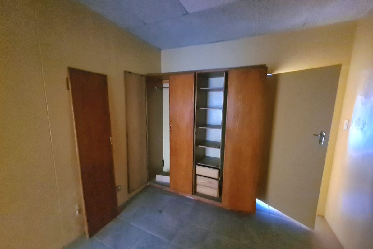 A bedroom featuring built-in wooden cupboards, tiled flooring, and a drop ceiling, presenting a dated interior ready for modernization.