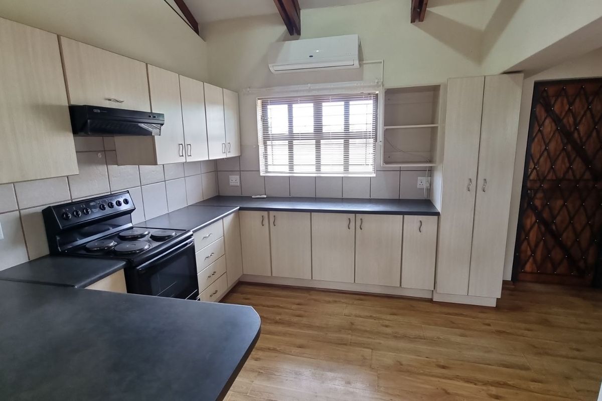 A functional kitchen featuring light-toned cabinetry, dark countertops, a built-in stove with extractor fan, and a wall-mounted air conditioning unit.