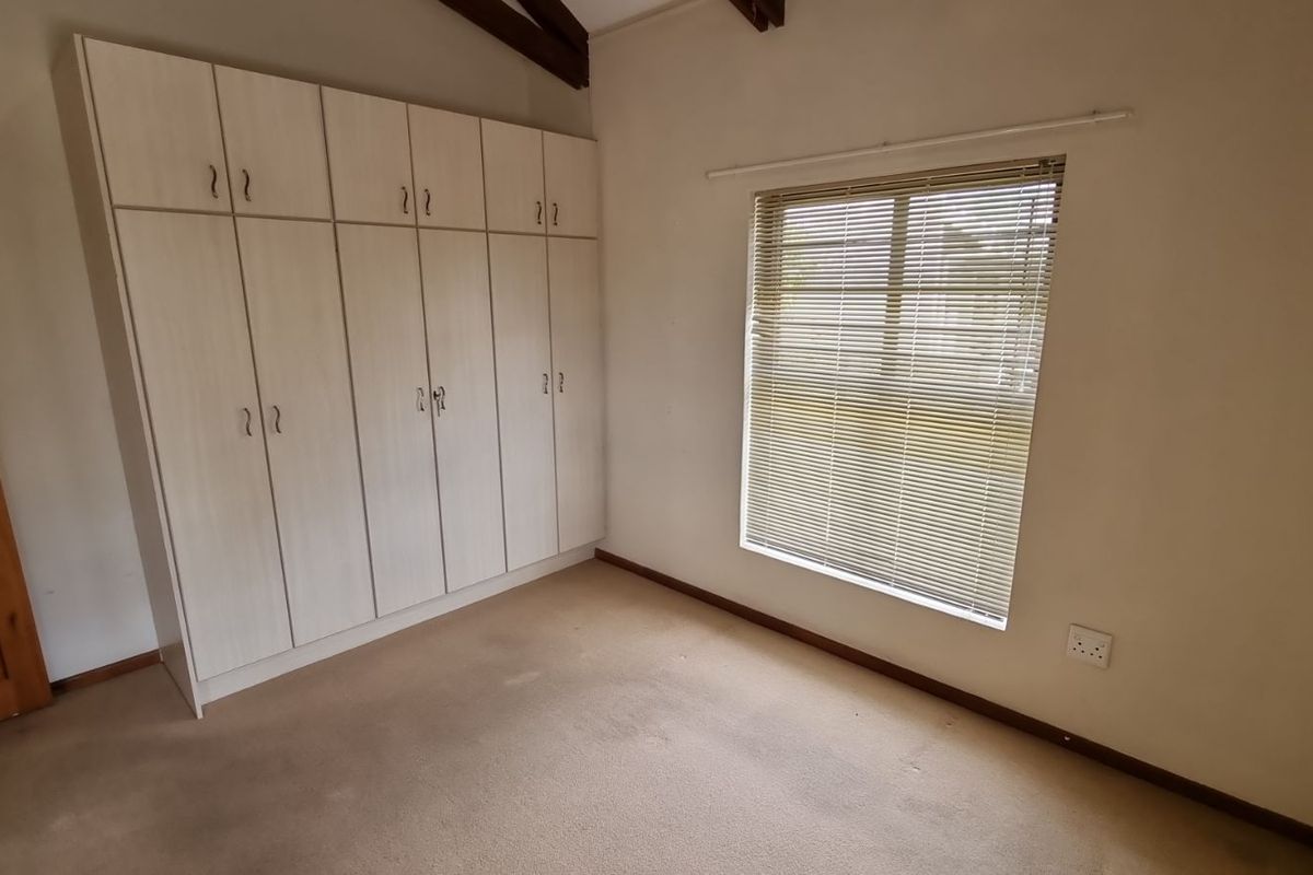 A bedroom featuring built-in cupboards, carpeted flooring, and a window with fitted blinds.