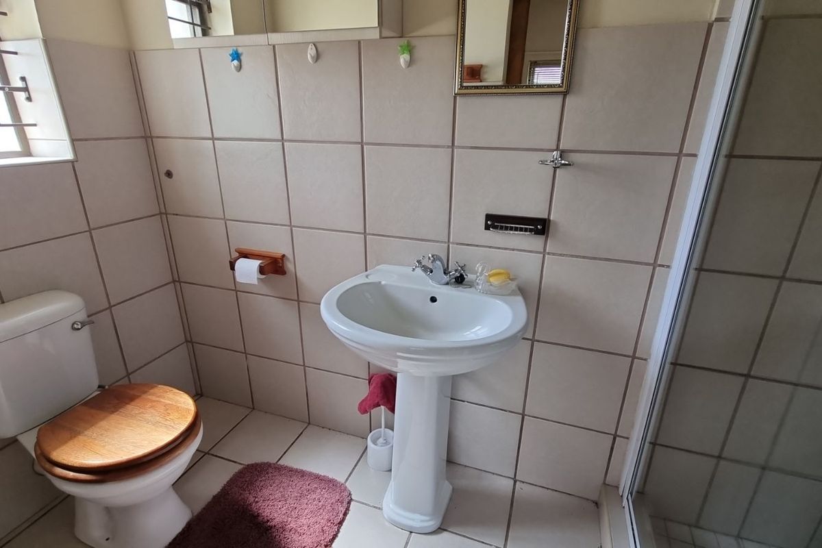 A functional bathroom featuring a pedestal basin, a standard toilet, and a shower enclosure with tiled walls and flooring.