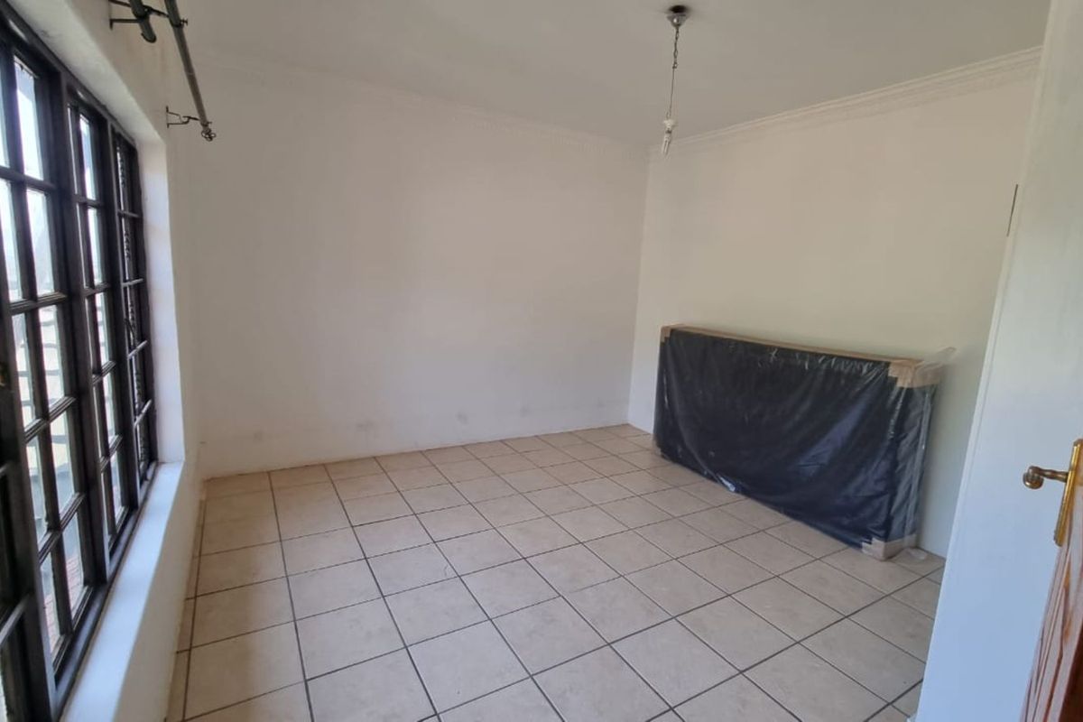 A vacant bedroom featuring tiled flooring, large multi-pane windows, and plain white walls, offering a blank canvas for personalization.
