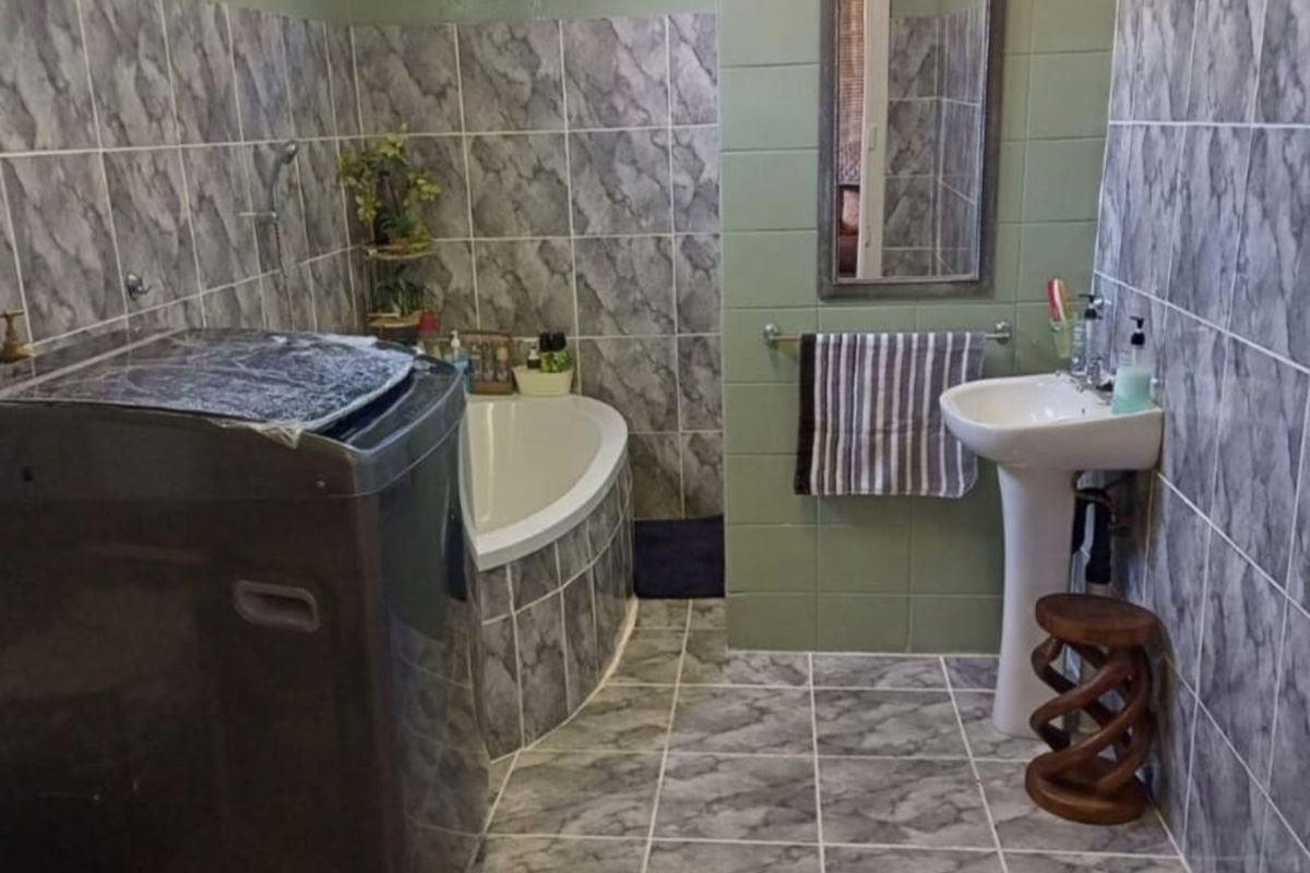 A functional bathroom featuring a corner bathtub, pedestal basin, and tiled finishes, with space for laundry appliances.