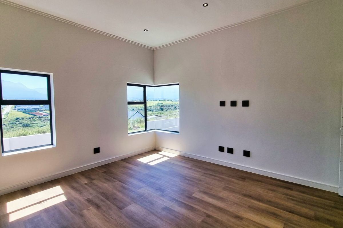 A bright, modern bedroom featuring wood-look flooring, recessed ceiling lighting, and corner windows offering scenic landscape views.