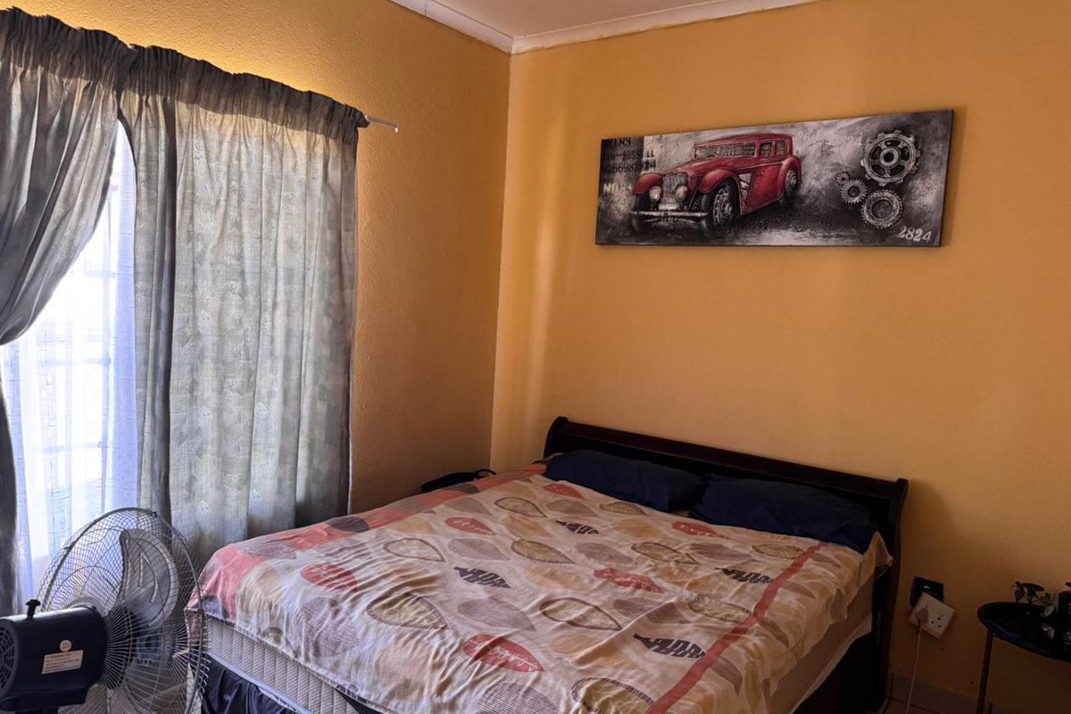 A standard bedroom featuring yellow painted walls, tiled flooring, and a window with curtain fixtures.