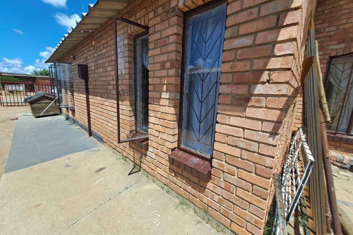 Exterior view of a brick house featuring metal security bars on windows and a concrete walkway along the side of the building.