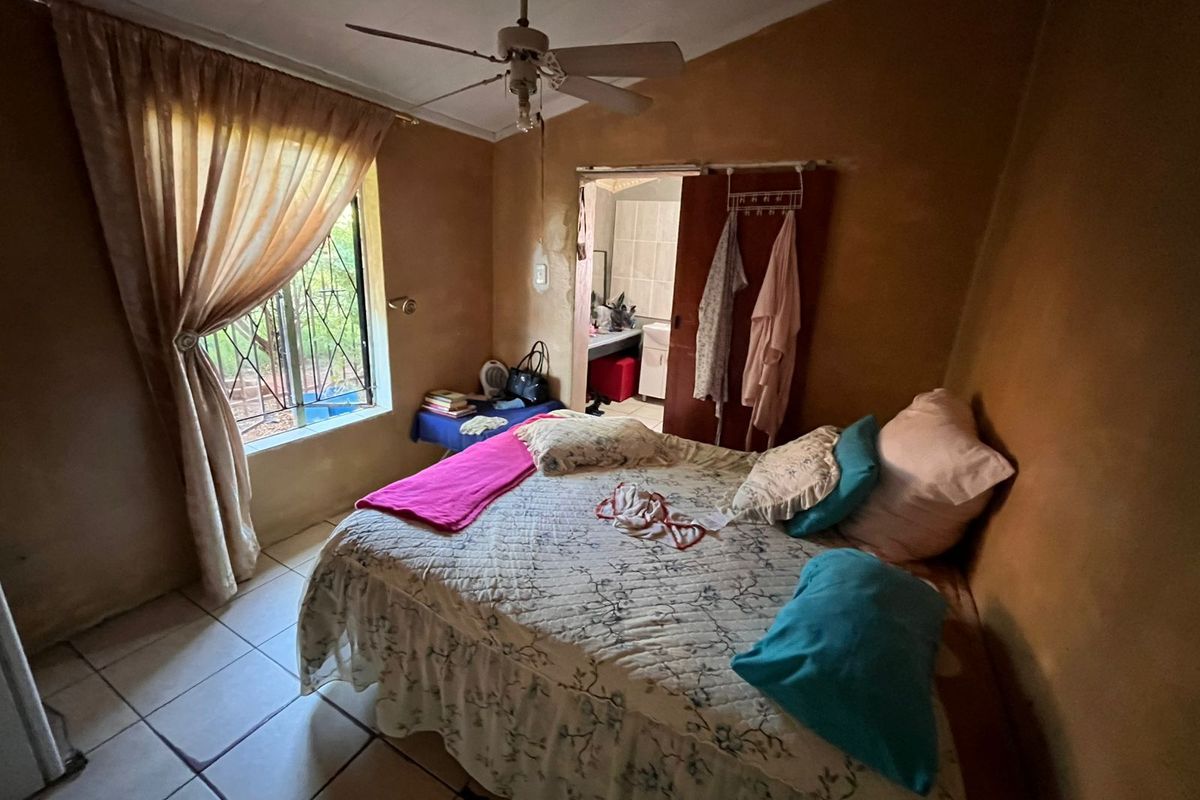 A bedroom featuring tiled flooring, a ceiling fan, and an en-suite bathroom access point with security bars on the window.