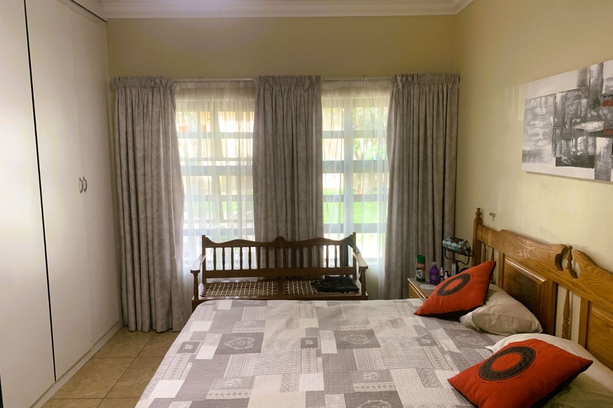 A well-lit bedroom featuring built-in floor-to-ceiling wardrobes, tiled flooring, and a wall-mounted air conditioning unit.
