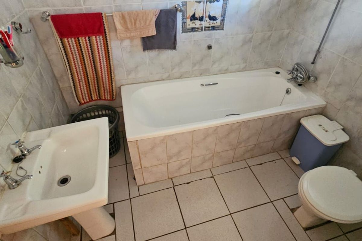 A dated bathroom featuring a standard bathtub, pedestal sink, and toilet with full-height wall tiling and ceramic floor tiles.