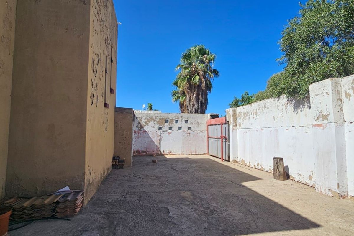 A rear exterior courtyard area featuring concrete paving and high perimeter boundary walls in need of maintenance and repainting.