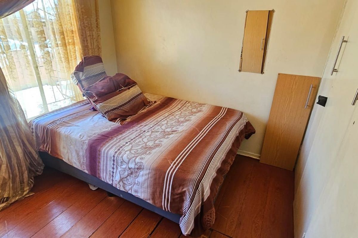 A compact bedroom featuring timber flooring, built-in cabinetry, and natural light from a large window.