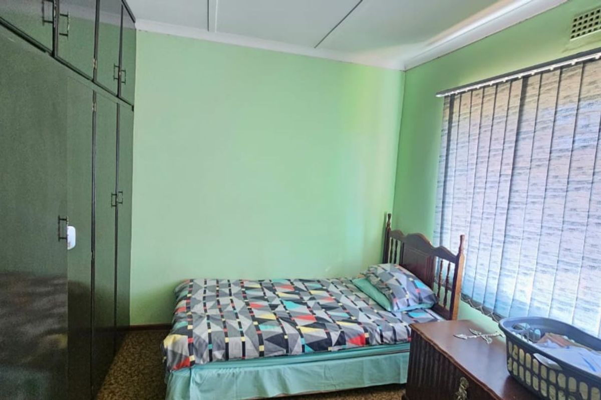 A bedroom featuring built-in dark cabinetry, carpeted flooring, and vertical window blinds.