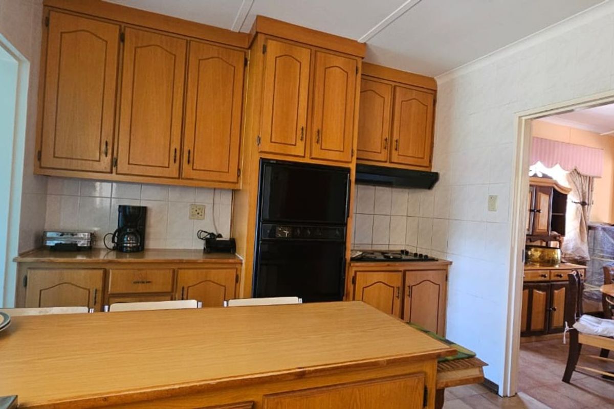 A functional kitchen featuring traditional timber cabinetry, built-in oven, and hob, with tiled splashbacks and a breakfast bar area.