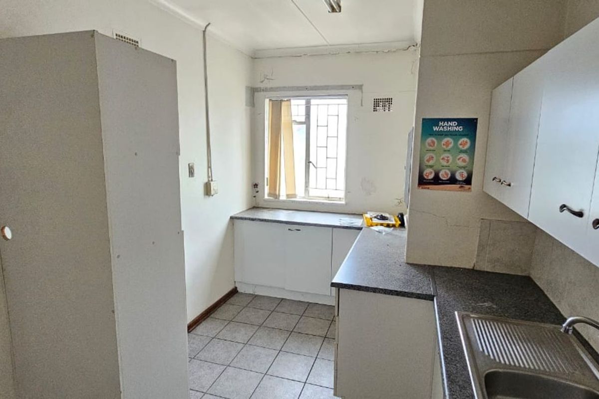 A functional office kitchenette featuring built-in cabinetry, a stainless steel sink, and tiled flooring, requiring cosmetic updates to modernize the space.