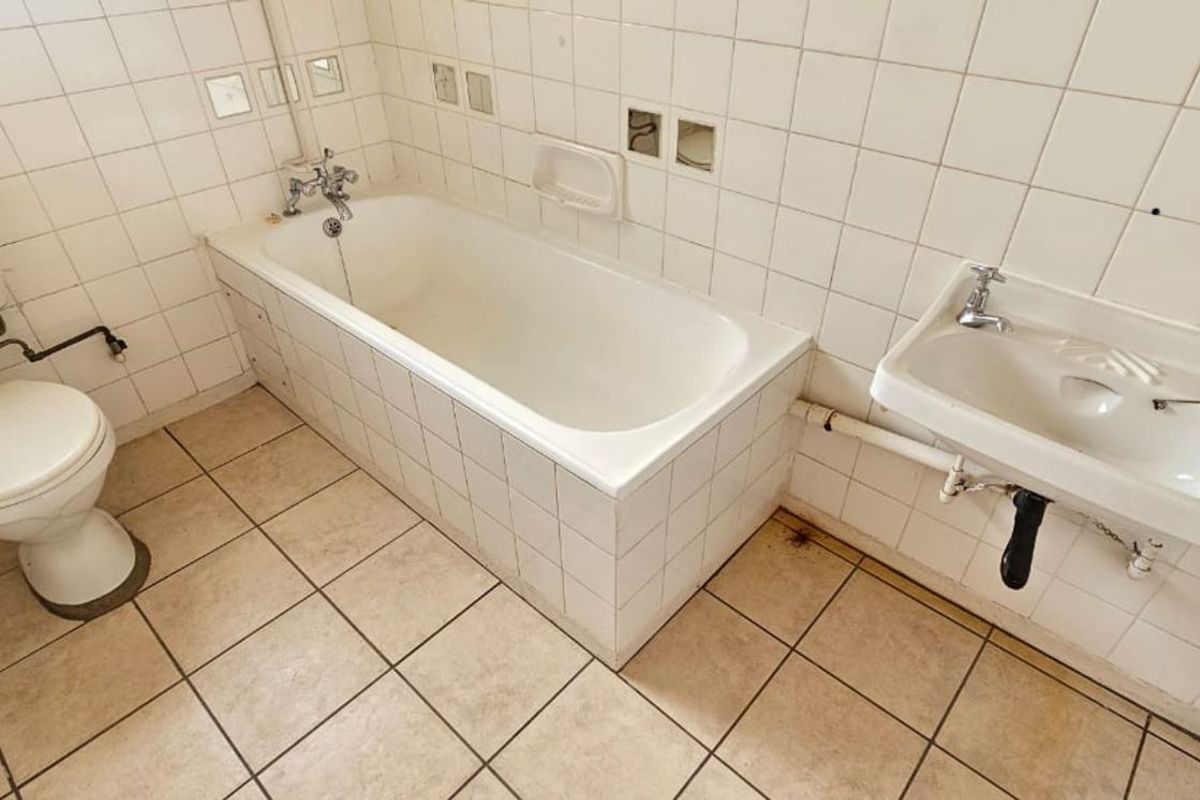 A dated bathroom featuring a standard bathtub, wall-mounted basin, and toilet with tiled walls and flooring, requiring modernization and maintenance.