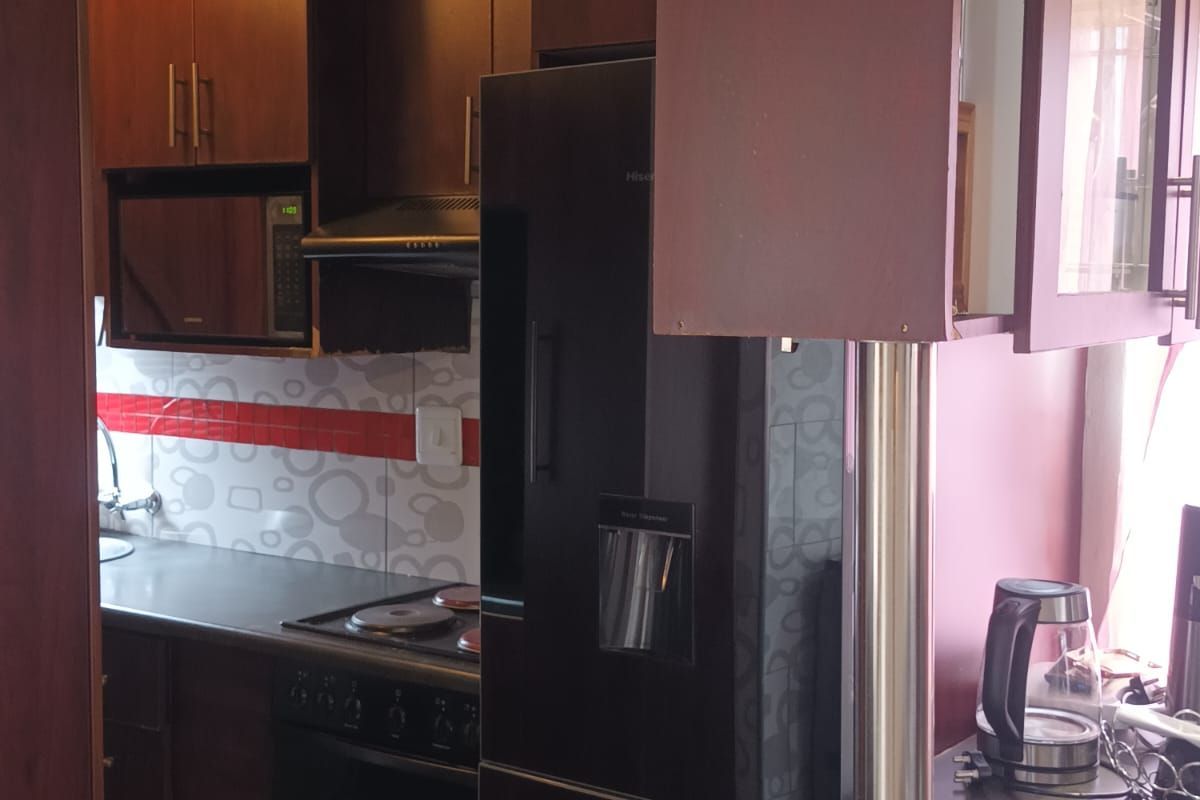 A compact kitchen featuring dark wood cabinetry, integrated oven and hob, tiled backsplash, and a breakfast bar counter.