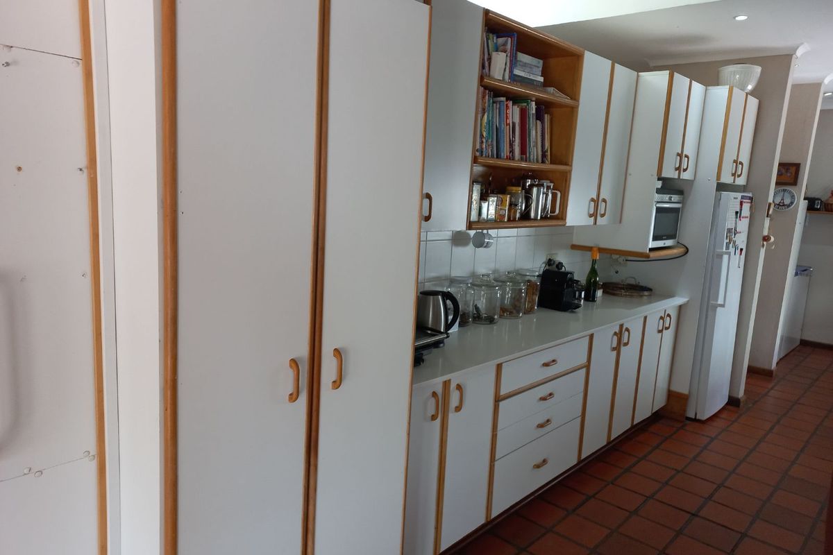 A functional kitchen featuring white cabinetry with timber trim, tiled flooring, and integrated storage space, offering a classic and practical layout.