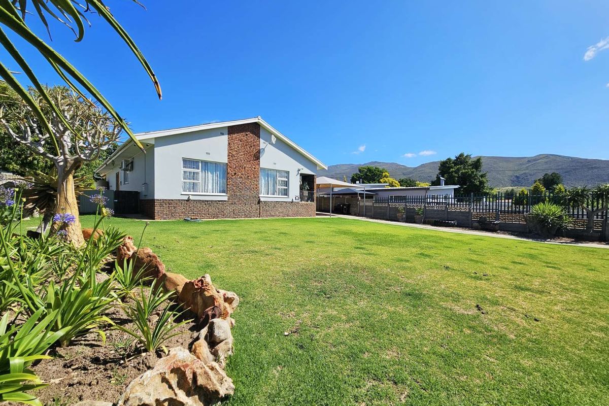 A well-maintained rear garden featuring a spacious lawn, established landscaping, and a clear view of the surrounding mountain range.