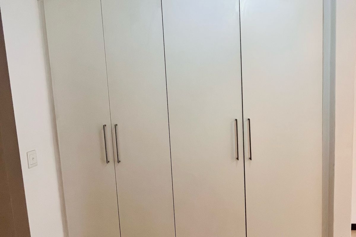 A bedroom featuring built-in white cabinetry with modern handles and tiled flooring.
