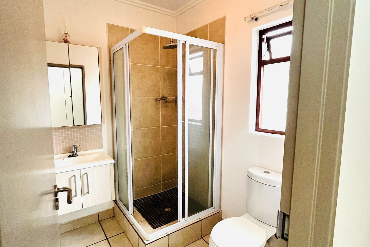 A functional bathroom featuring a corner shower enclosure, a vanity with integrated basin, and a standard toilet with tiled flooring.