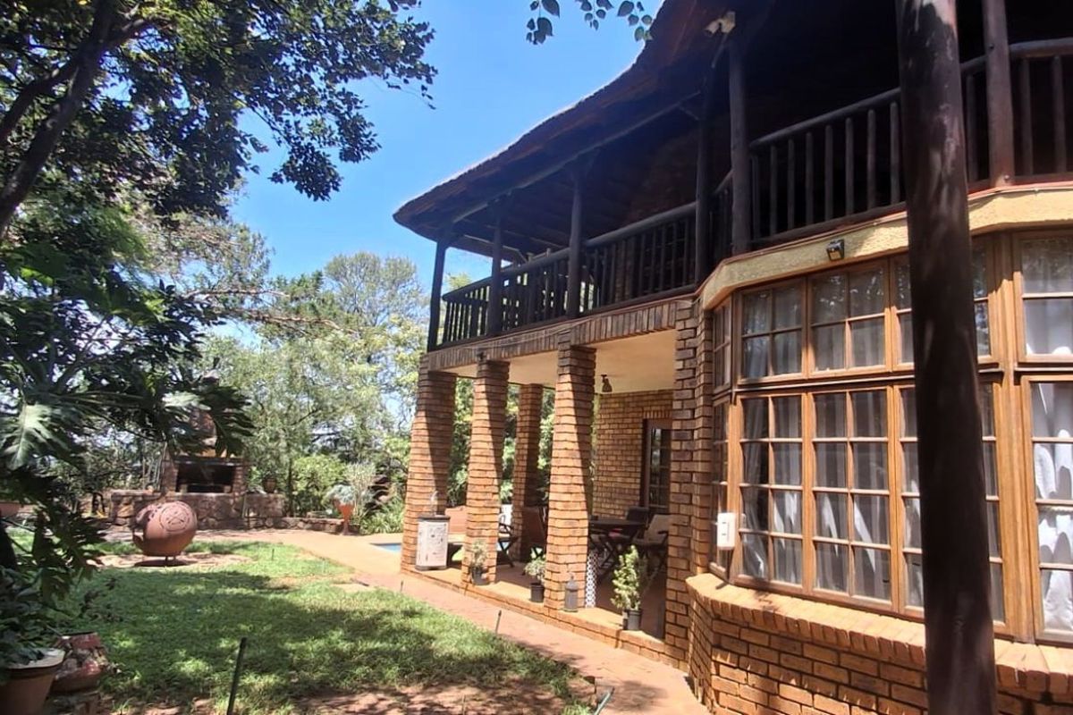 A view of the rear exterior of the house, featuring a brick facade, a covered patio, and a balcony overlooking the garden area.