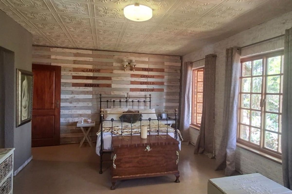 A rustic-style bedroom featuring a decorative pressed metal ceiling, timber-clad feature wall, and large windows allowing natural light.
