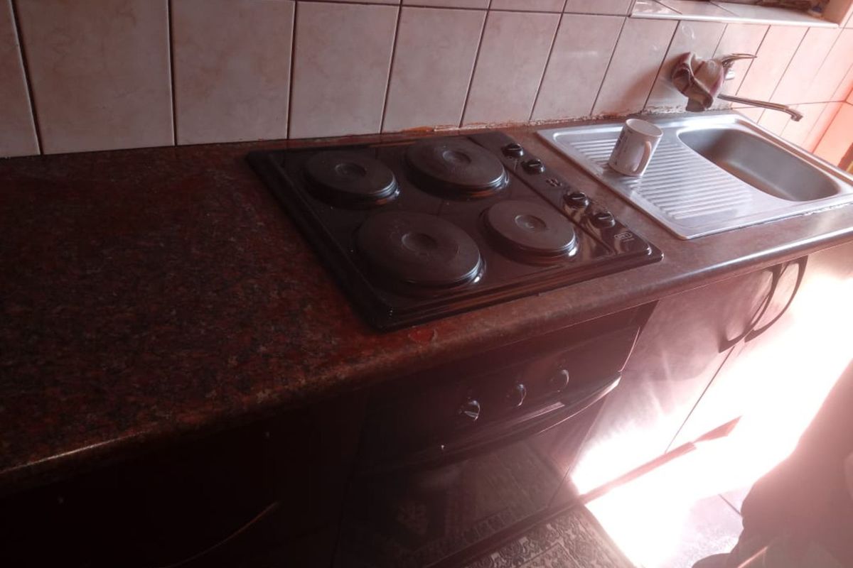 Compact kitchen area featuring a built-in electric hob, oven, and stainless steel sink with tiled backsplash.