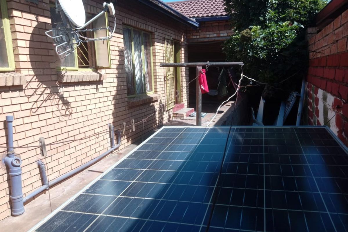 Rear exterior view of the property featuring a brick facade, solar panel installation, satellite dish, and a functional utility area.