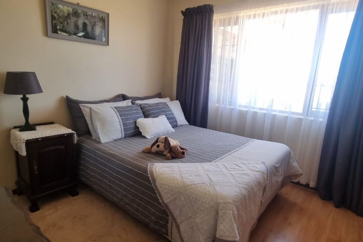 A well-lit bedroom featuring laminate flooring, large window with curtain tracks, and neutral wall finishes.