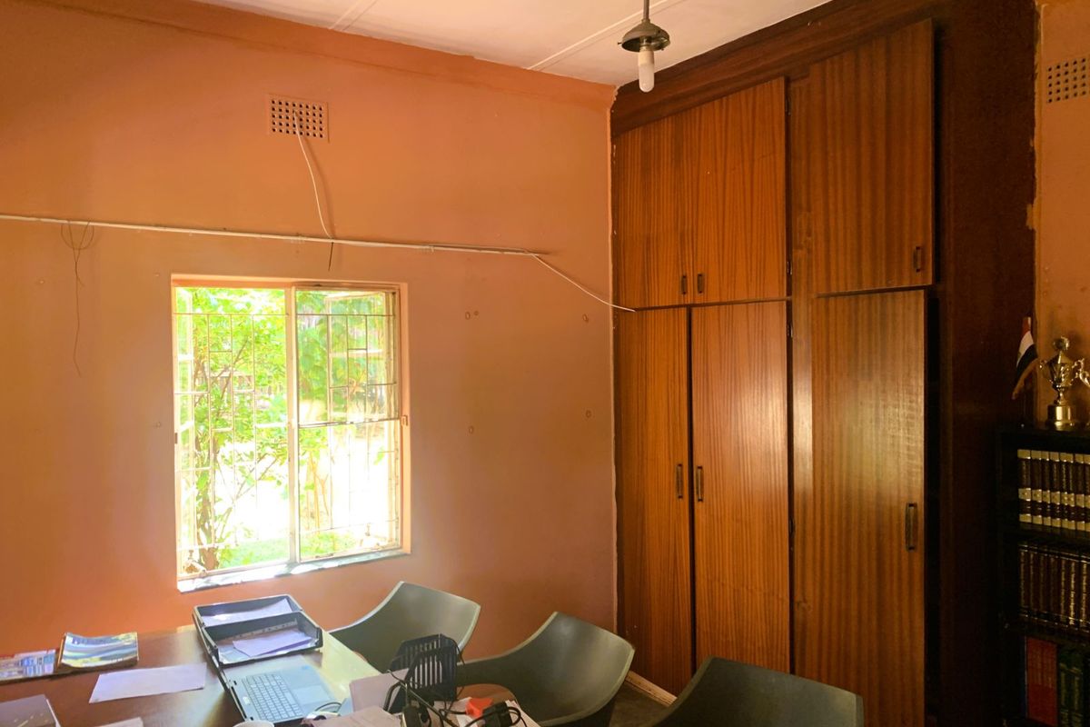 A bedroom featuring built-in wooden cupboards, a window with security bars, and exposed surface-mounted electrical wiring.