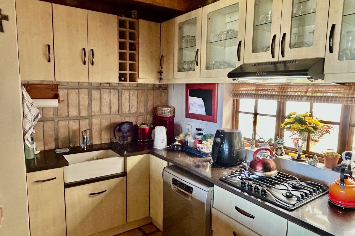 A rustic farm-style kitchen featuring light wood cabinetry, a farmhouse sink, granite countertops, and a built-in gas hob with an extractor fan.