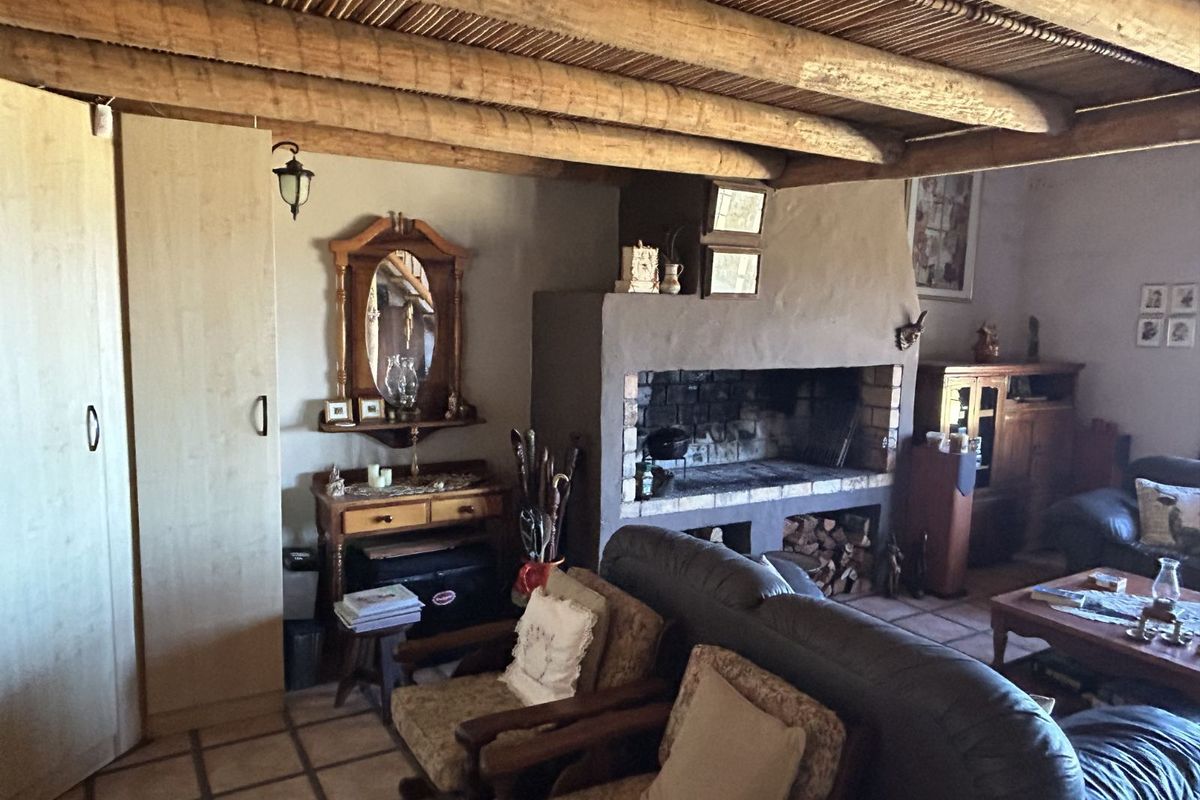 Rustic living room featuring a large built-in masonry fireplace, exposed timber beam ceiling with reed infill, and tiled flooring.
