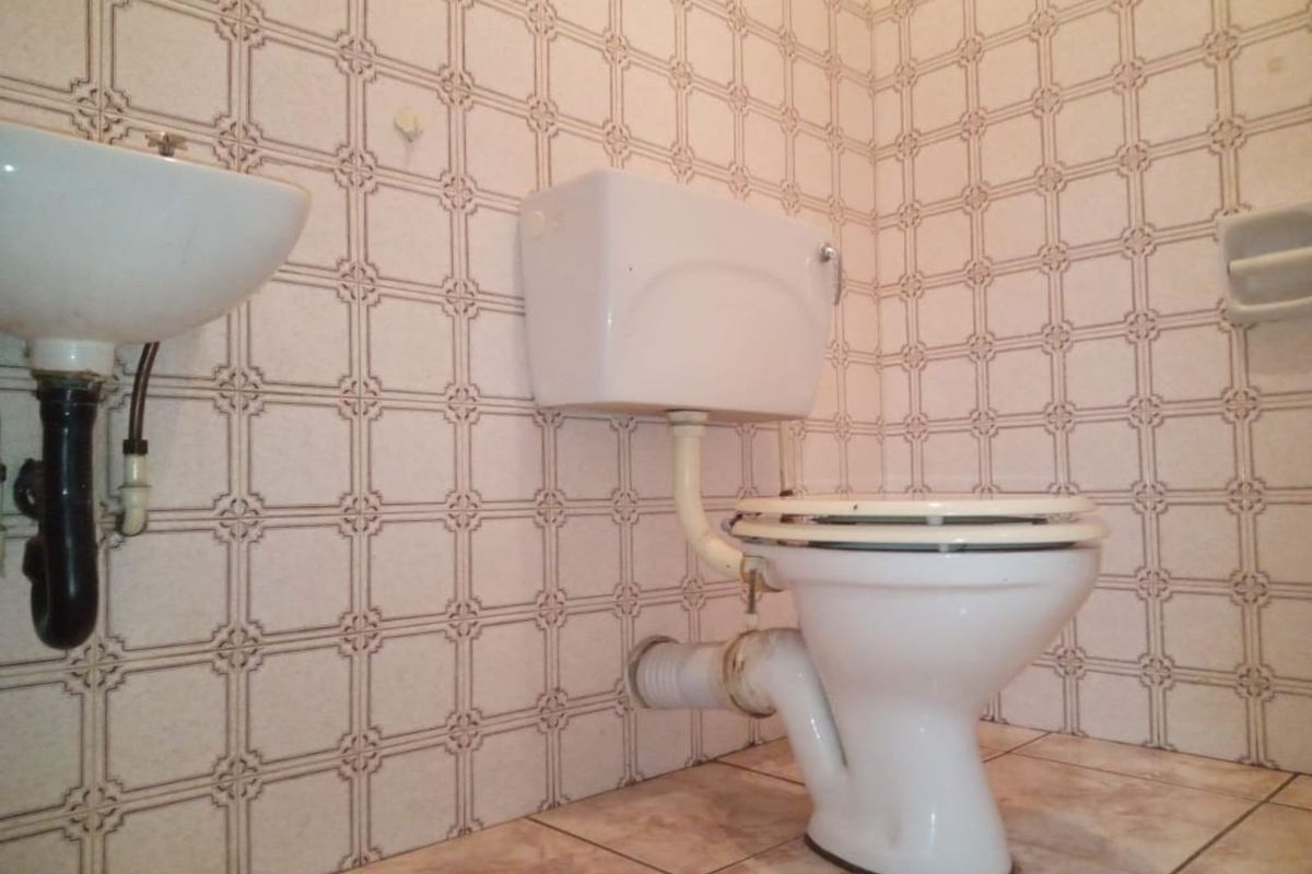 A compact bathroom featuring a wall-mounted basin and a traditional low-level flush toilet with dated ceramic wall and floor tiling.