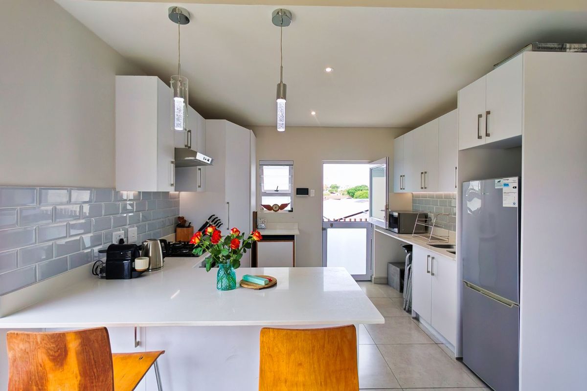 Modern kitchen featuring white cabinetry, stone countertops, subway tile backsplash, and a breakfast bar island with pendant lighting.