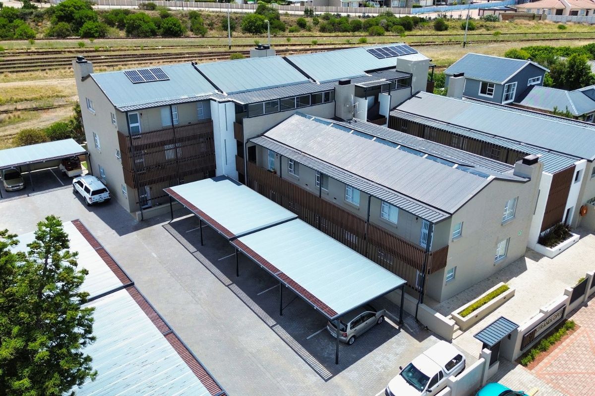 Aerial view of a modern apartment complex featuring covered parking bays, metal roofing, and solar panels.