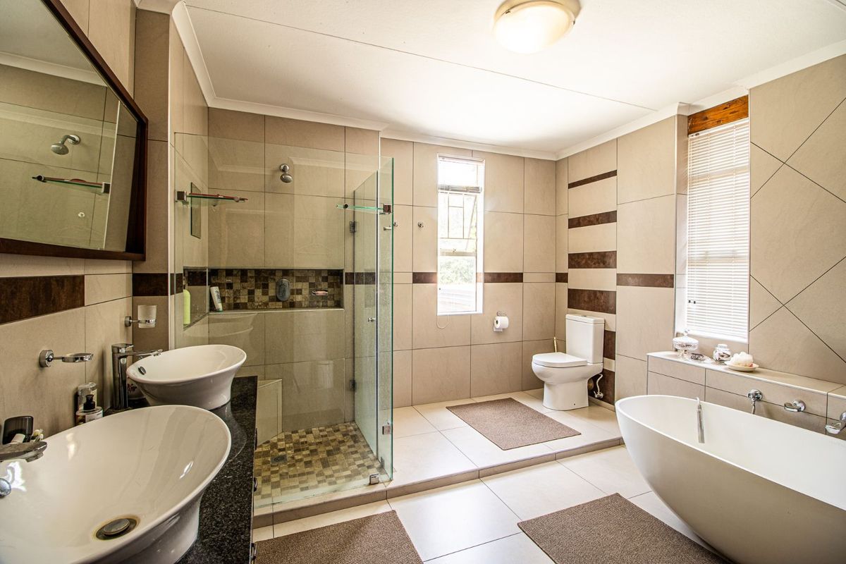 Spacious modern bathroom featuring a glass-enclosed walk-in shower, a freestanding bathtub, dual vessel sinks on a granite vanity, and neutral floor-to-ceiling tiling.