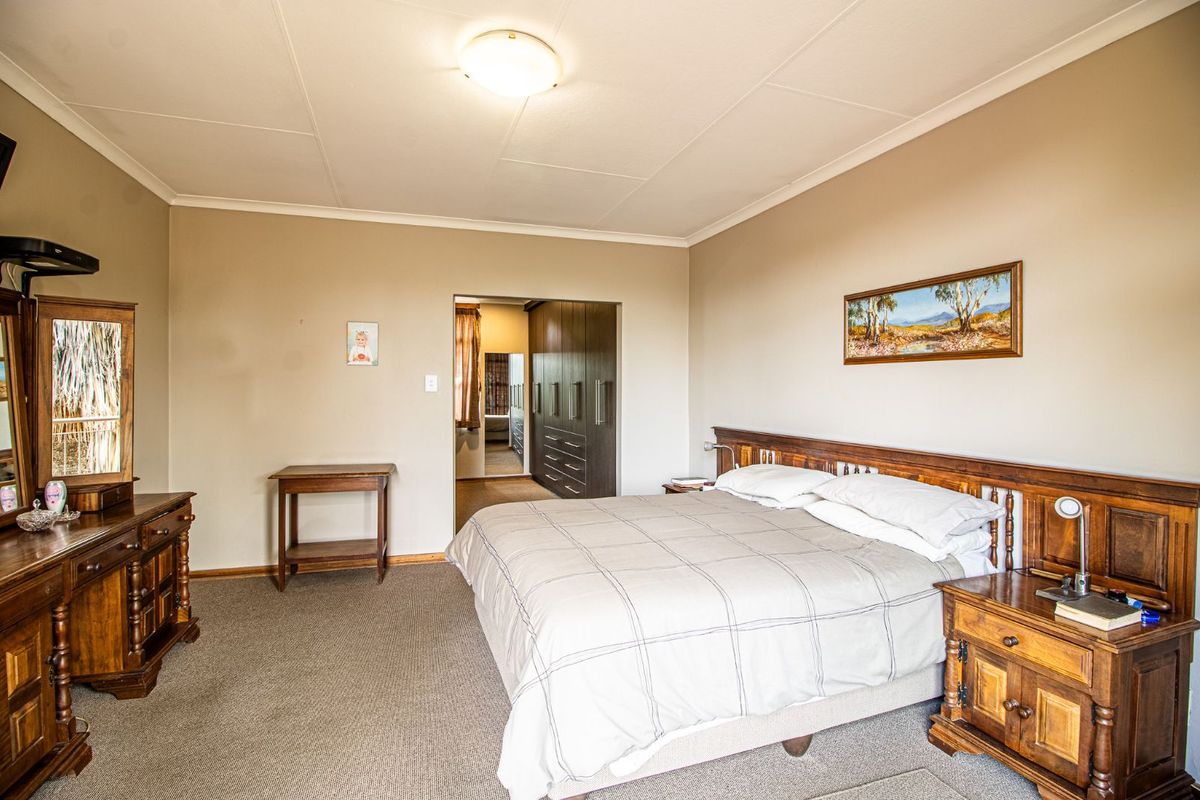 Spacious bedroom featuring neutral wall tones, carpeted flooring, and a built-in wardrobe area accessible through a doorway.