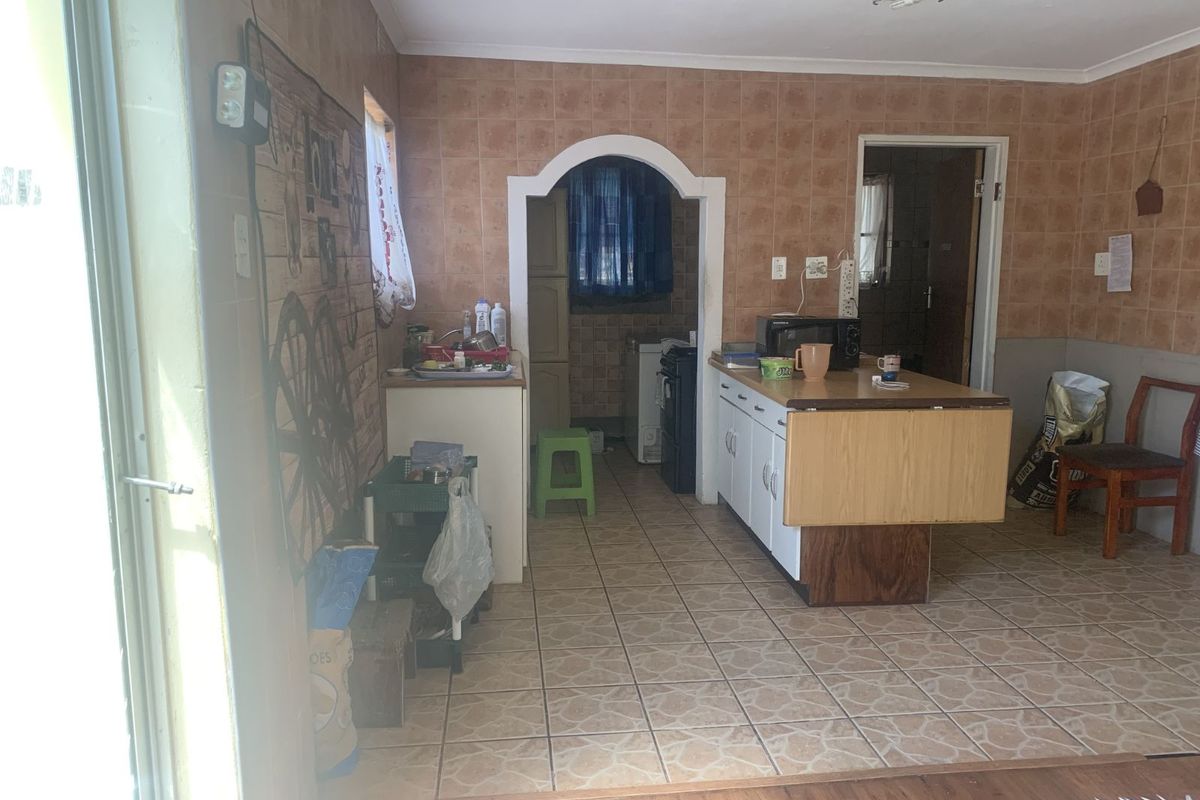A dated kitchen area featuring tiled walls, a central island unit, and an arched doorway leading to a secondary prep or utility space.