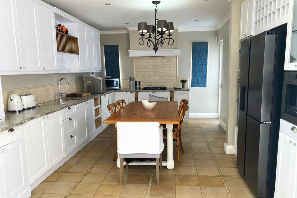 A well-appointed kitchen featuring white cabinetry, granite countertops, a subway tile backsplash, and a central dining area with tiled flooring.
