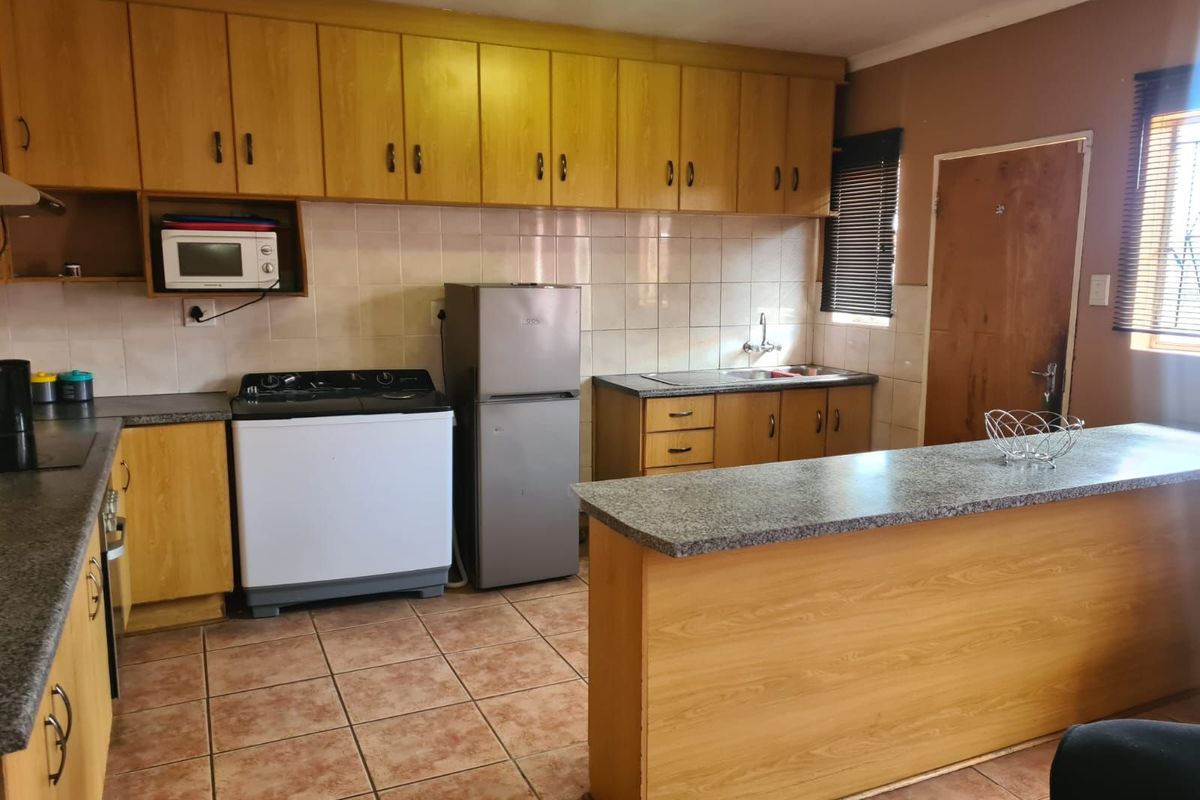 A functional kitchen featuring wood-look cabinetry, granite-style countertops, a breakfast bar, and tiled flooring with a neutral backsplash.