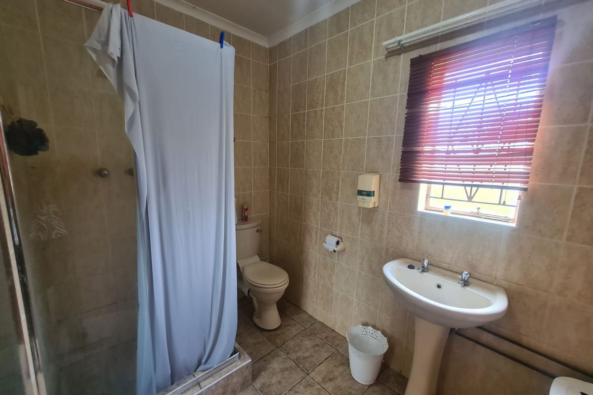 A functional bathroom featuring a pedestal basin, a toilet, and a glass-enclosed shower with neutral wall and floor tiling.